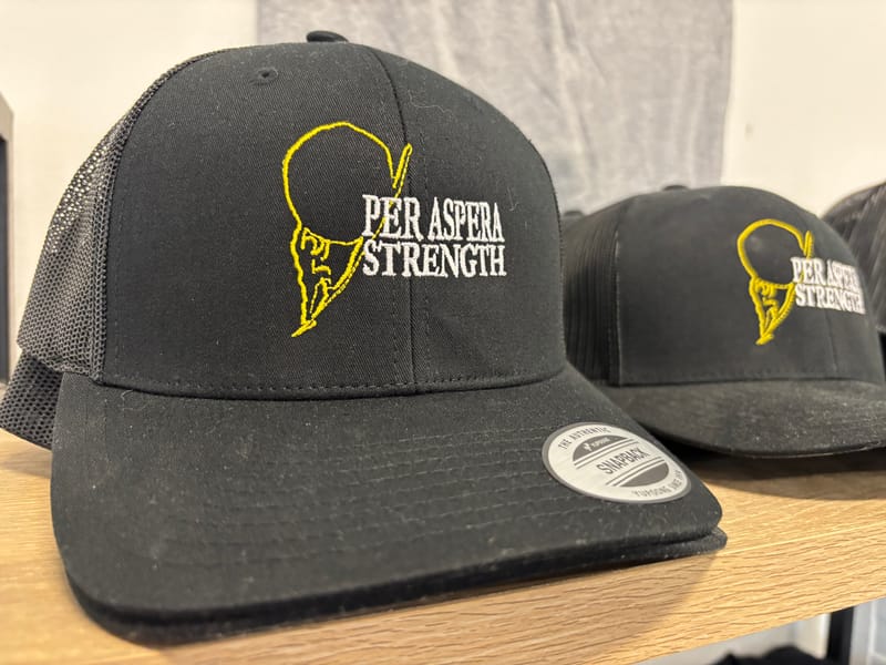 Black Per Aspera Strength snapback trucker cap with the yellow embroidered Sisyphus logo