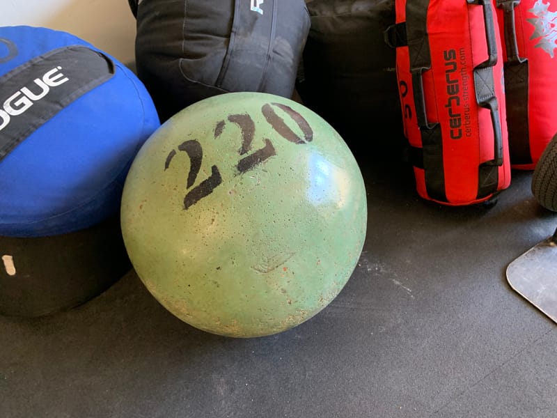 220 lb atlas stone in a green finish between sandbags in the gym