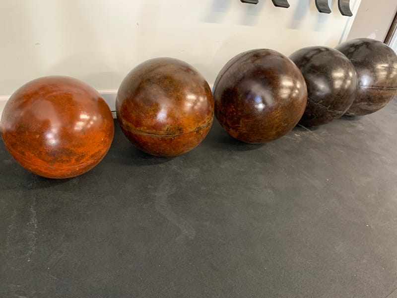 A graded set of five finished atlas stones lined up on the gym floor, from red-brown through black