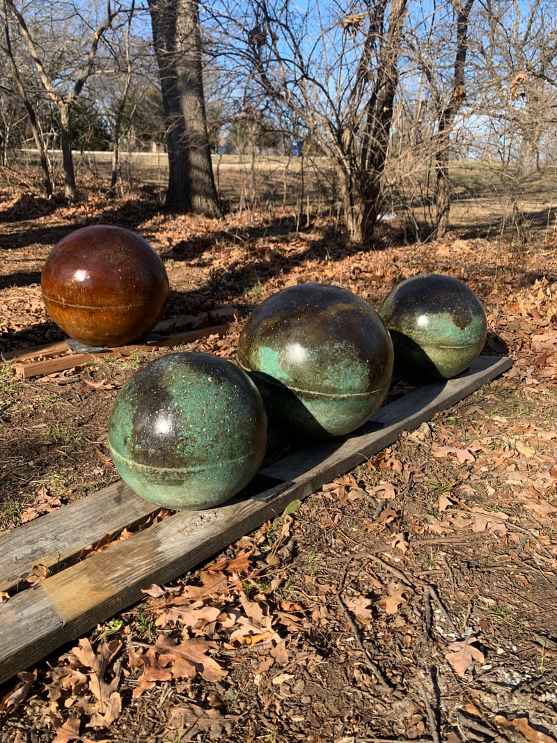 Three green and black marbled atlas stones and one amber stone curing on a plank outdoors